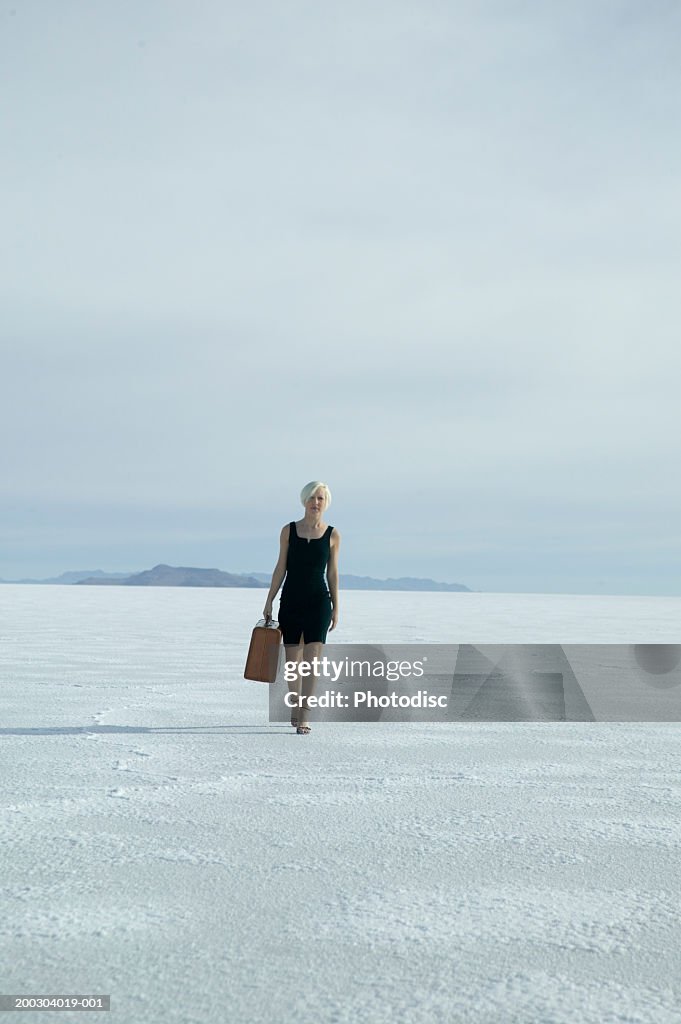 Woman in dress carrying suitcase in desert