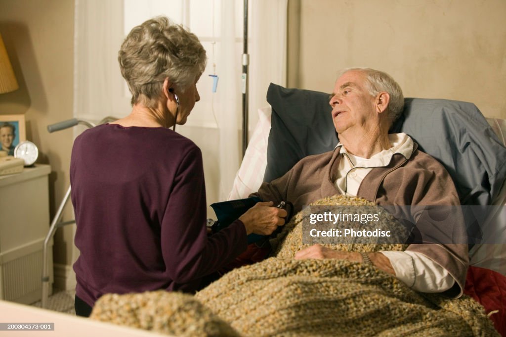 Senior doctor checking blood pressure of senior man in bed in retirement home