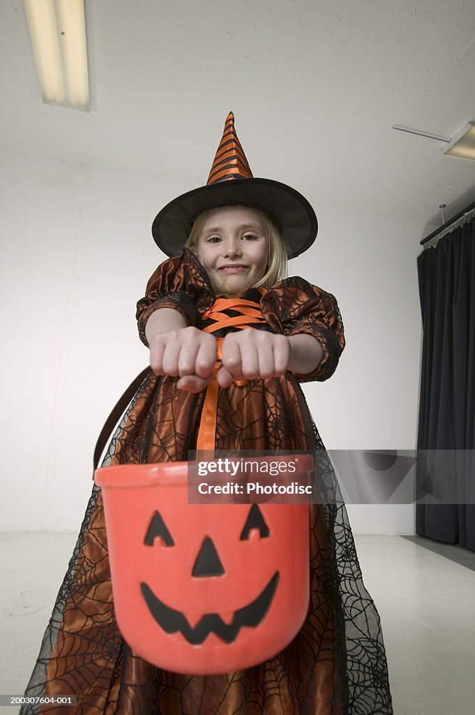 Girl (8-9) in witch costume holding Halloween bucket in studio, low angle view