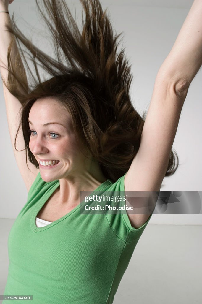 Woman jumping with arms outstretched, posing in studio, portrait