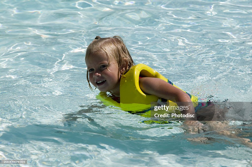 Girl (4-5) in life-jacket floating in pool