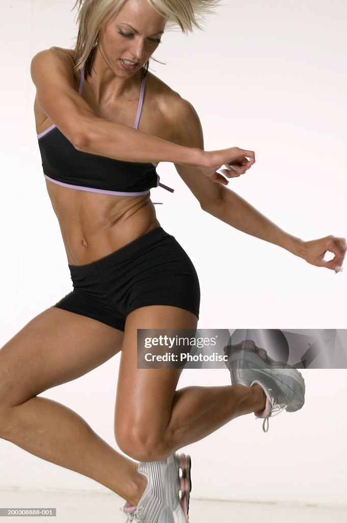 Woman in sports top and shorts jumping, in studio