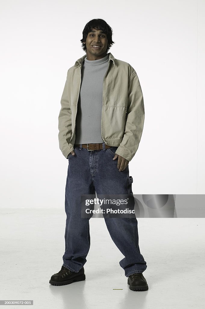 Young man with hands in pockets, standing in studio, portrait