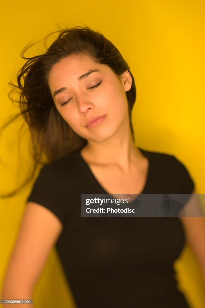 Young woman in black, with eyes closed, against yellow background