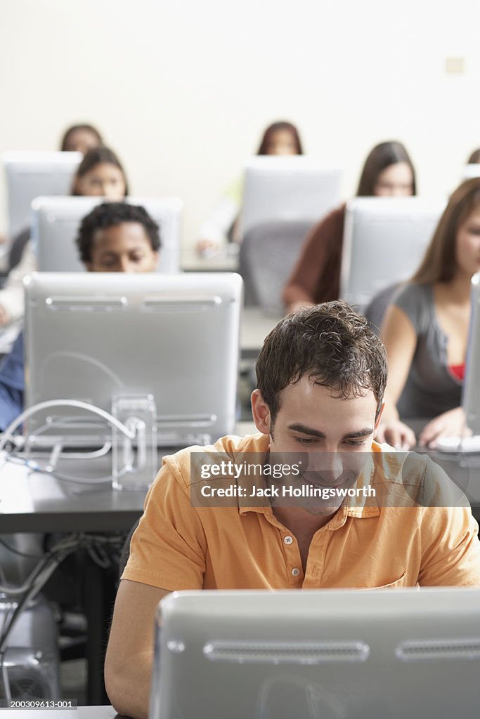 Group of young people sitting in front of computer monitors in a classroom