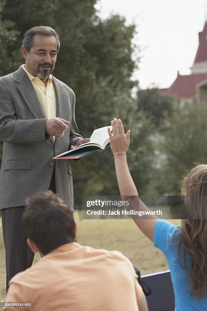 Male lecturer teaching  students on a lawn