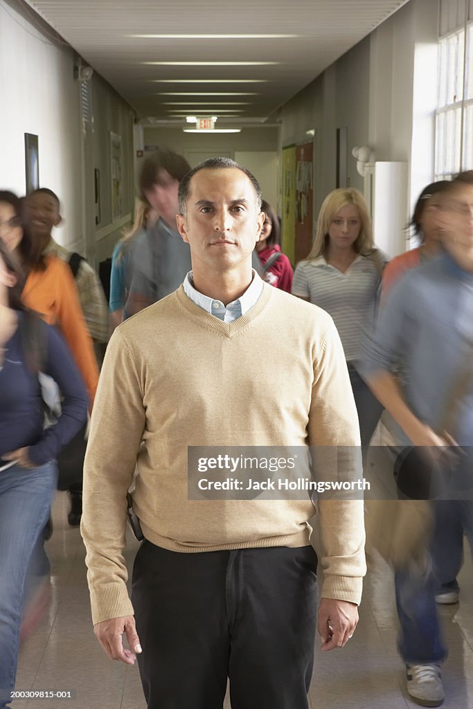 Portrait of a male lecturer standing in a corridor with students walking beside him