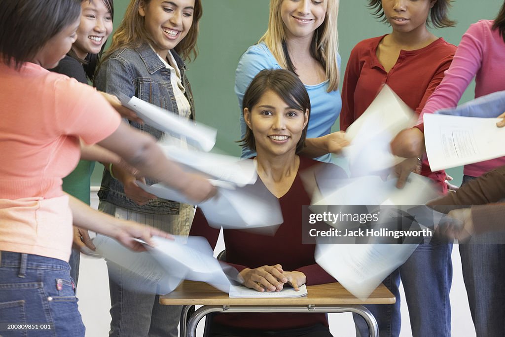 Group of teenagers holding sheets of paper in front of their lecturer in a classroom