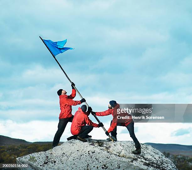 three male hikers raising flag on rock - elmos superheroes visit top of rock stockfoto's en -beelden