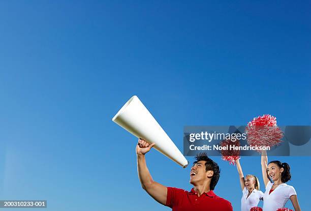 male cheerleader using megaphone, two female cheerleaders behind - asian cheerleaders stock-fotos und bilder