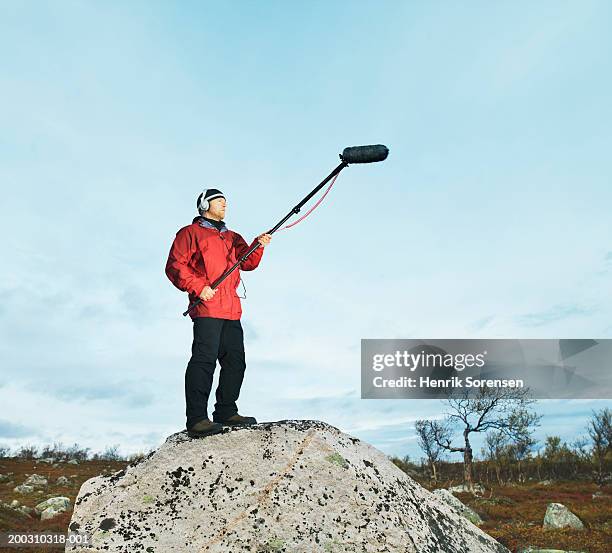 man on rock holding boom microphone, wearing headphones - girafe photos et images de collection