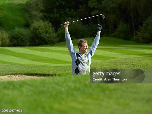 male golfer standing in bunker holding golf club, arms raised, smiling - sand trap imagens e fotografias de stock