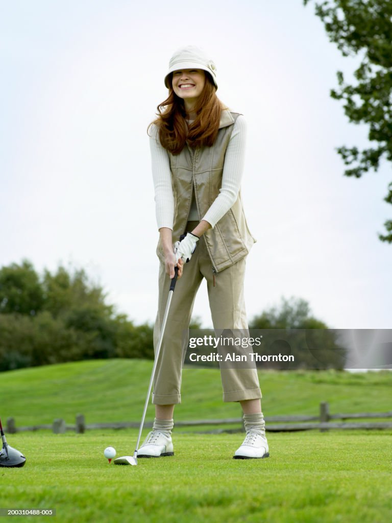 Female golfer preparing to hit ball, smiling