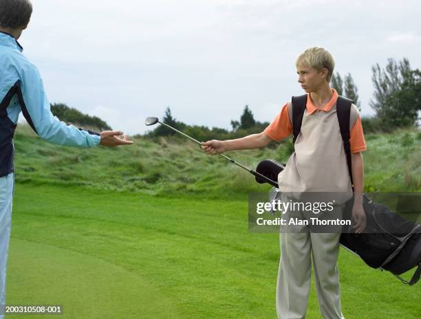 male teenage caddy (13-15) giving golf club to man - golf caddy stock-fotos und bilder