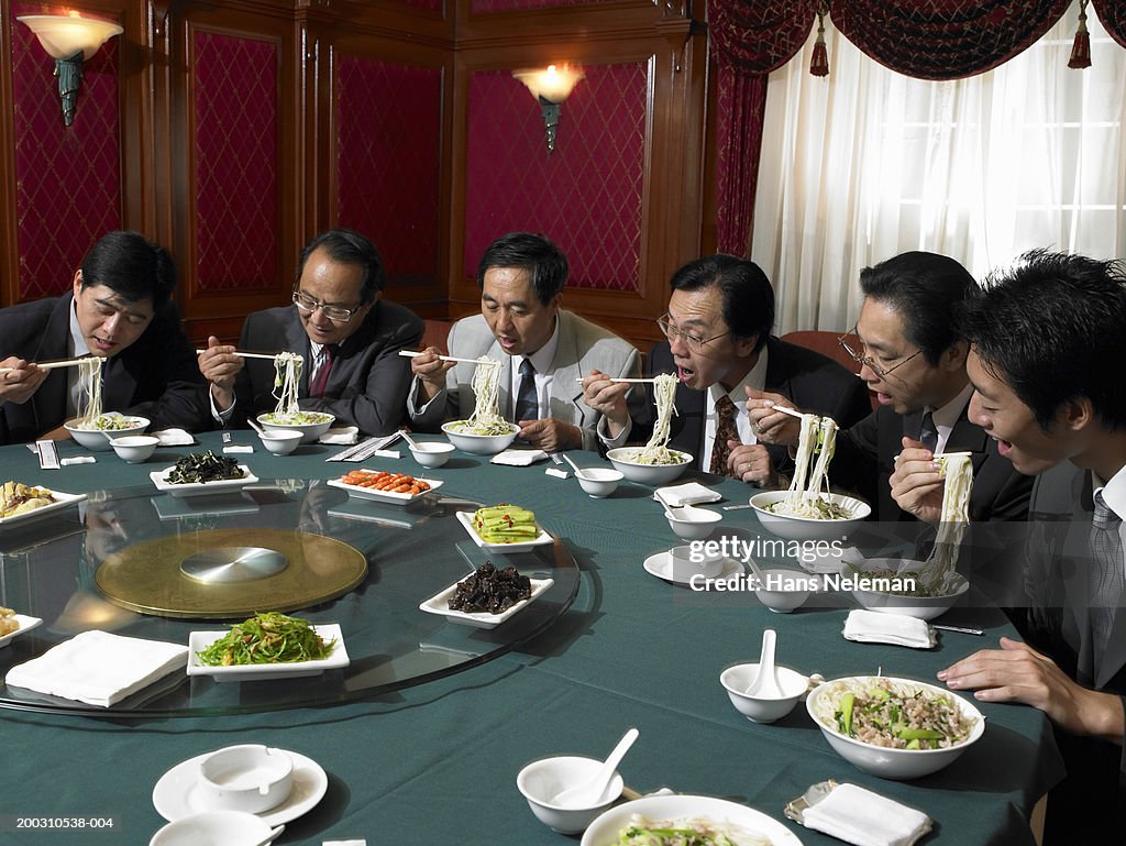 Businessmen at banquet table eating noodles