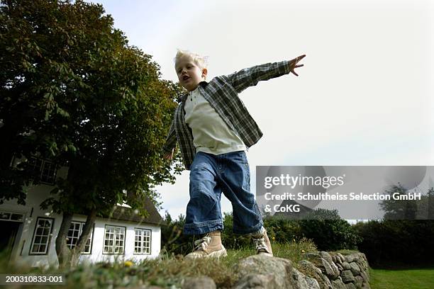 boy (4-6) running around garden with arms outstretched, low angle view - balancieren mauer stock-fotos und bilder