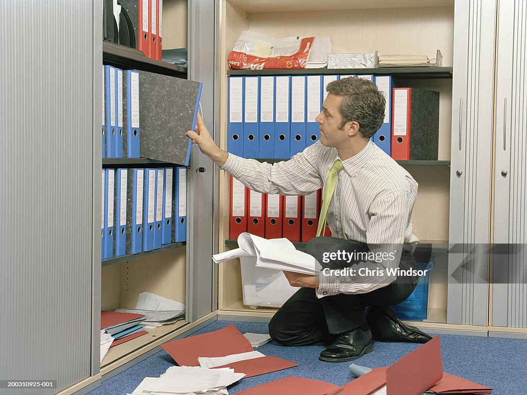Businessman kneeling on floor, selecting file from cupboard