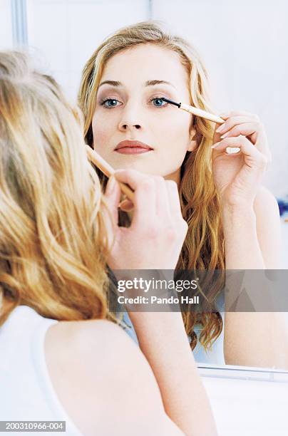 young woman applying mascara in mirror (focus on reflection) - bathroom closeup stockfoto's en -beelden