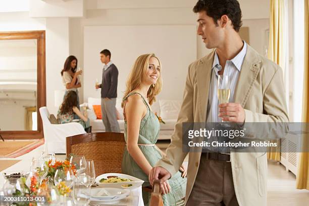 woman smiling at man standing by dining table, friends in background - flirten stockfoto's en -beelden