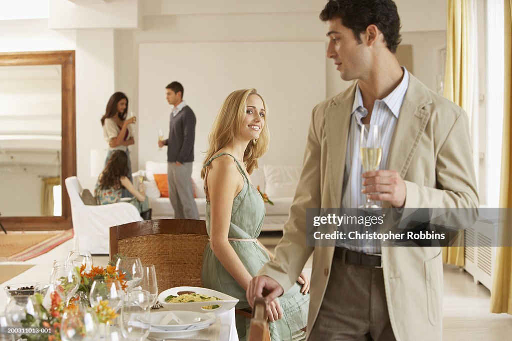 Woman smiling at man standing by dining table, friends in background