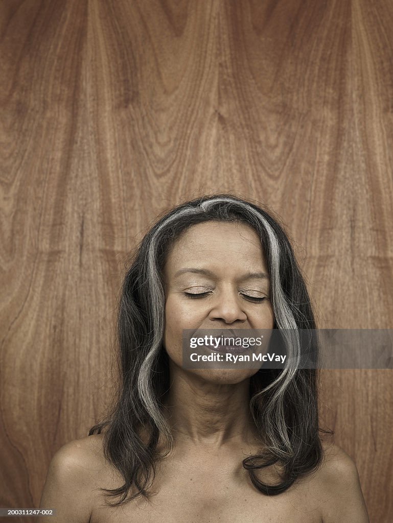 Senior woman against wood panelling, eyes closed, smiling