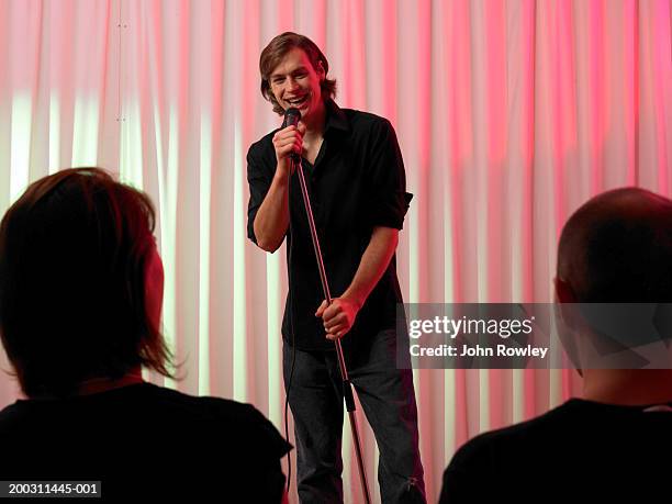 young man holding microphone facing audience, smiling - comedian mic stock pictures, royalty-free photos & images