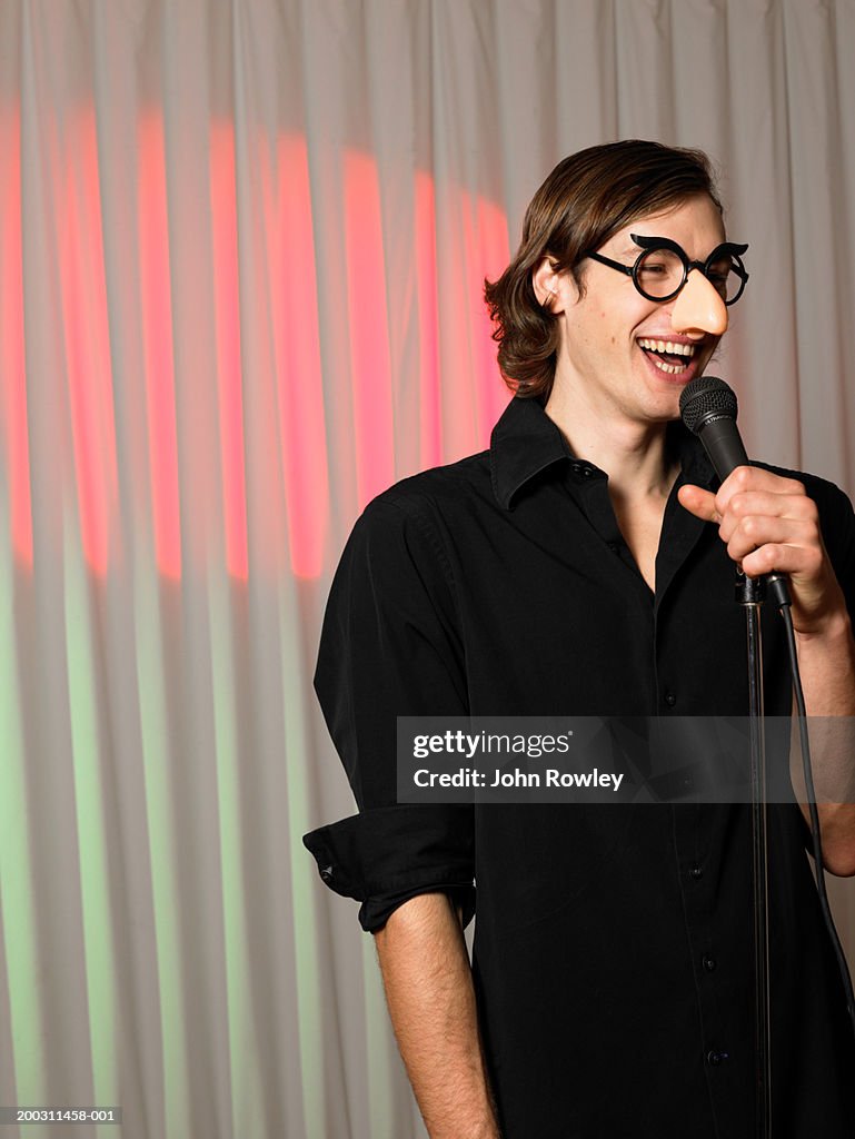 Man wearing joke nose and glasses, holding microphone, smiling