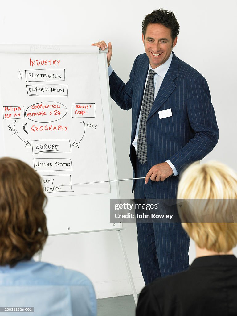 Businessman giving presentation, smiling, colleagues in foreground