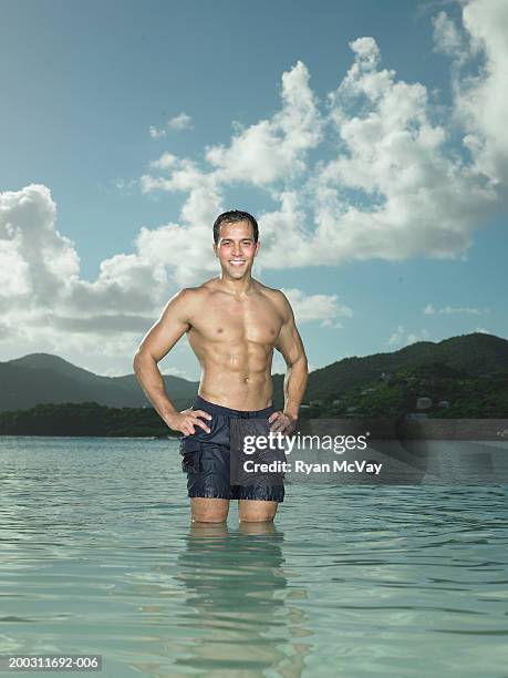 man standing in sea, hands on hips, smiling, portrait - wade stock pictures, royalty-free photos & images