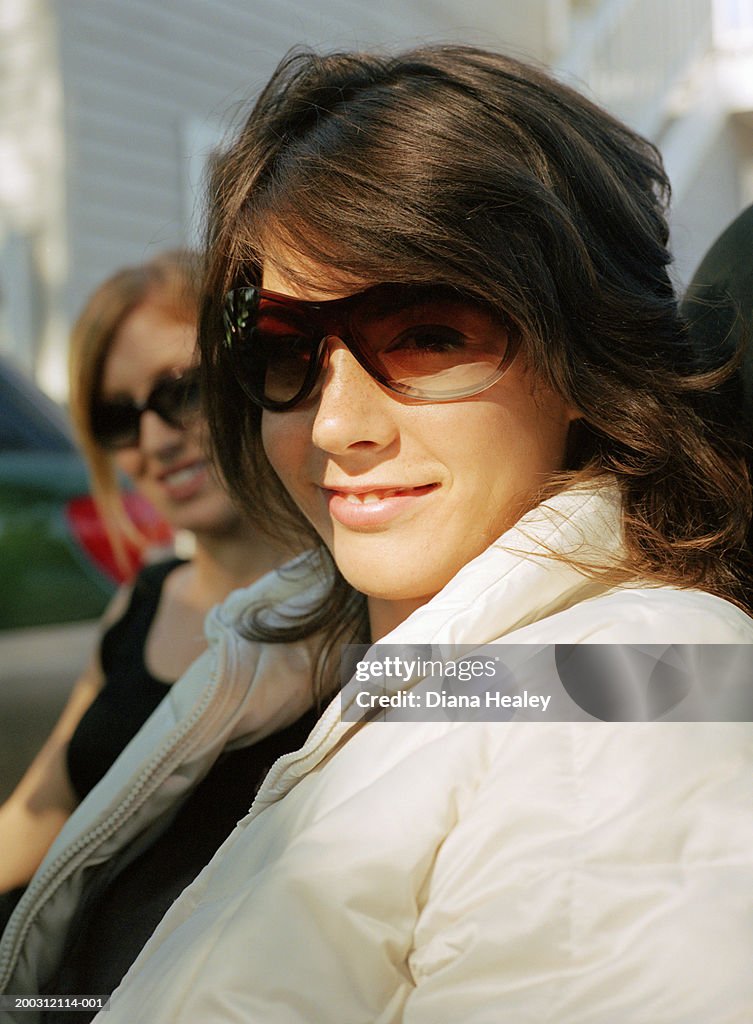 Two young women wearing sunglasses in car, smiling