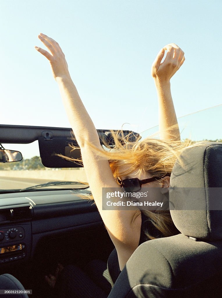 Young woman in car with arms outstretched