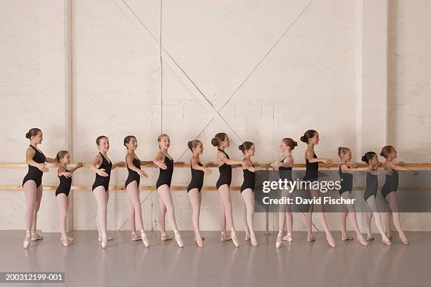 girls (8-13) in ballet class, holding bar in ballet pose, side view - bale imagens e fotografias de stock