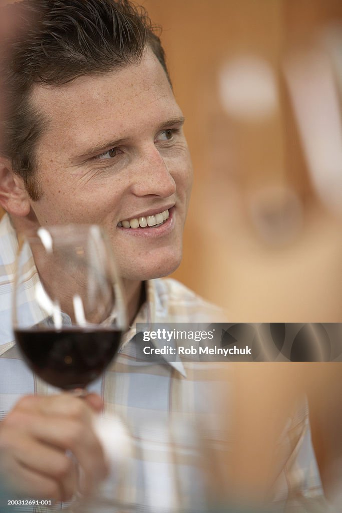 Young man holding glass of red wine, smiling