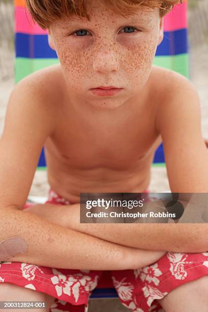 boy (6-8) sitting with folded arms, leaning on knees, portrait - red hair boy and freckles stock-fotos und bilder