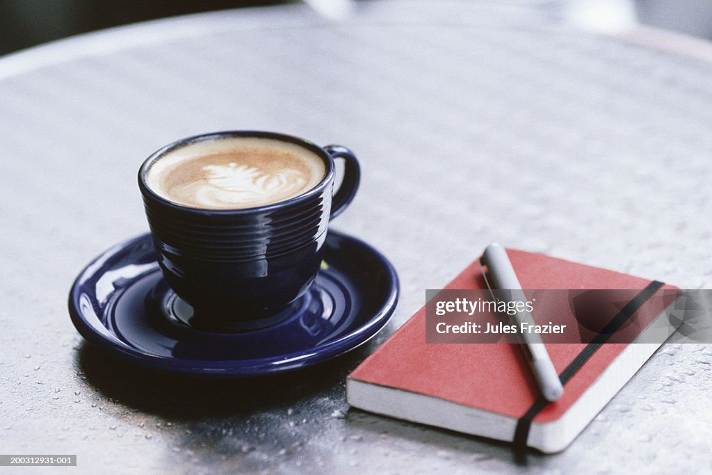 Cup of coffee, notebook and pen lying on table