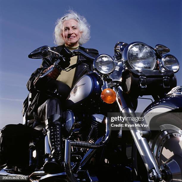 senior woman wearing leathers sitting on motorcycle, posing in studio, portrait, low angle view - frau motorrad stock-fotos und bilder