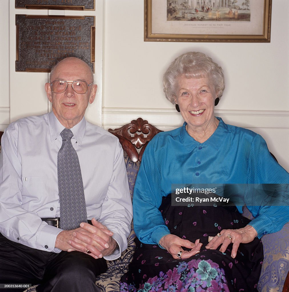 Senior couple sitting side by side on sofa in living room, portrait