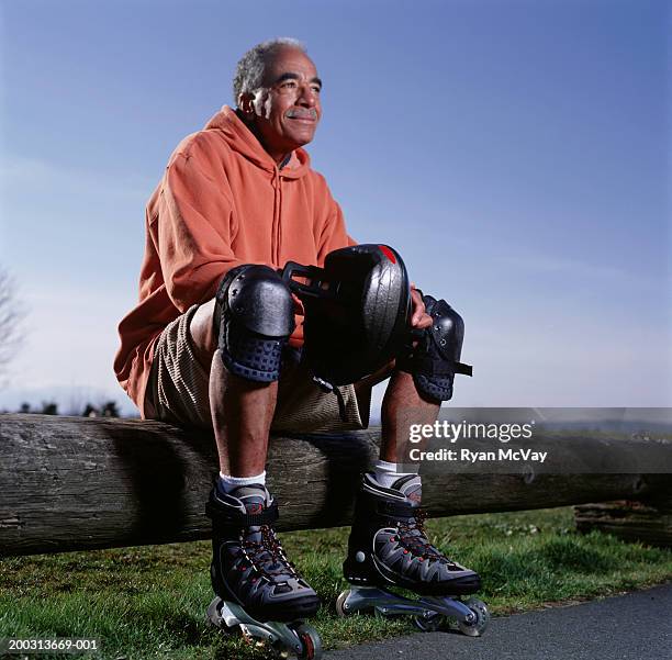 man wearing inline-skates sitting on log fence in park, portrait, low angle view - kniebeschermer stockfoto's en -beelden