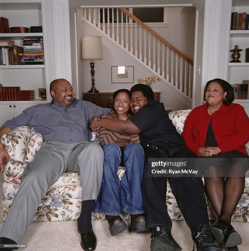 Two parents with teenage son and daughter (16-17), sitting on sofa in living room, portrait