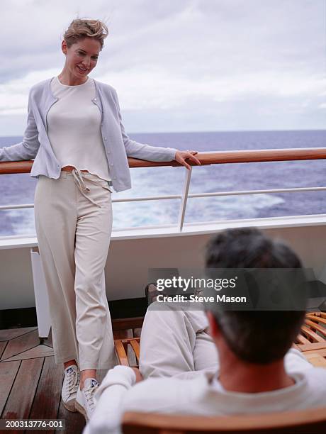 woman standing by railing, man sitting on deckchair on cruise ship - boat deck stock-fotos und bilder