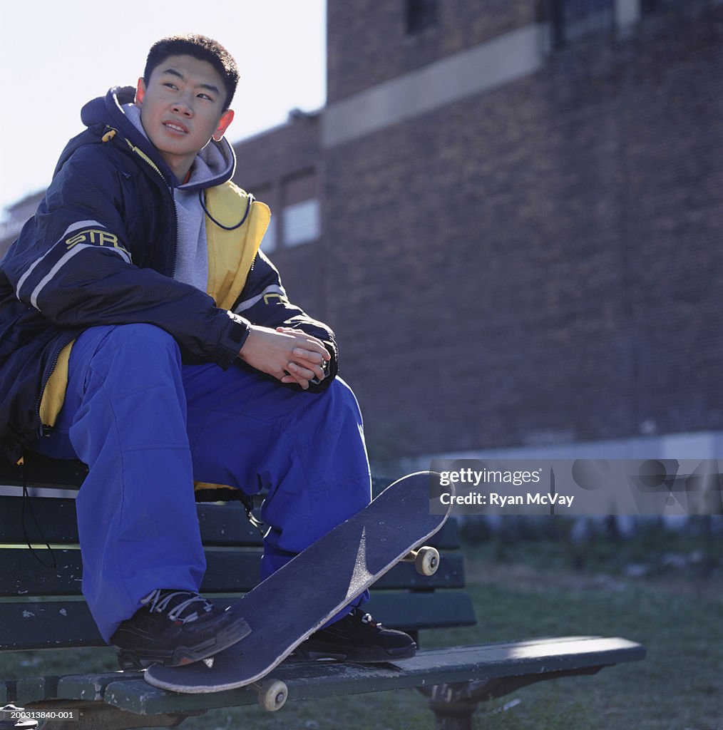 Teenage (14-15) skater sitting on wooden bench, low angle view