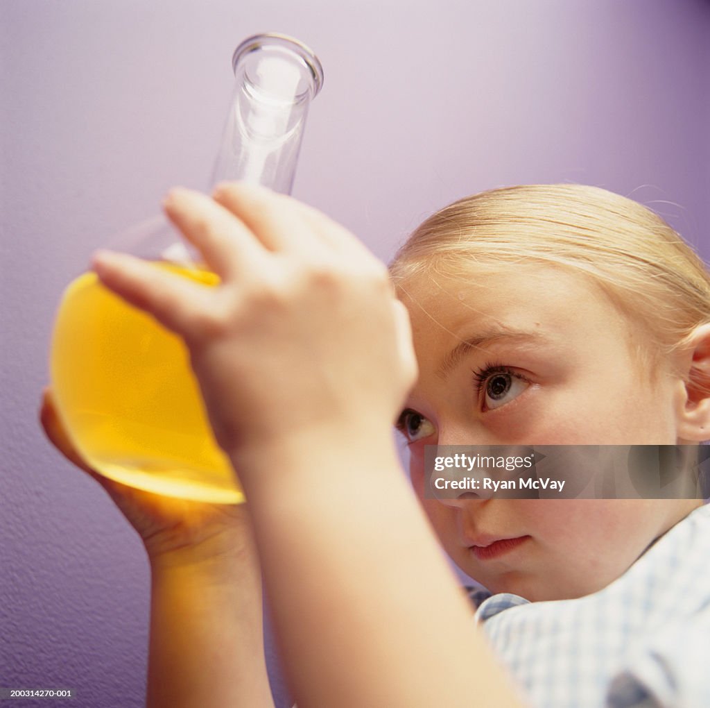 Girl (6-7), holding flask, looking at liquid inside, posing in studio, portrait