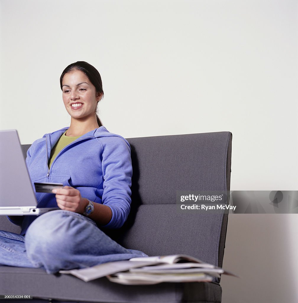 Young woman sitting on couch, using laptop, posing in studio, portrait