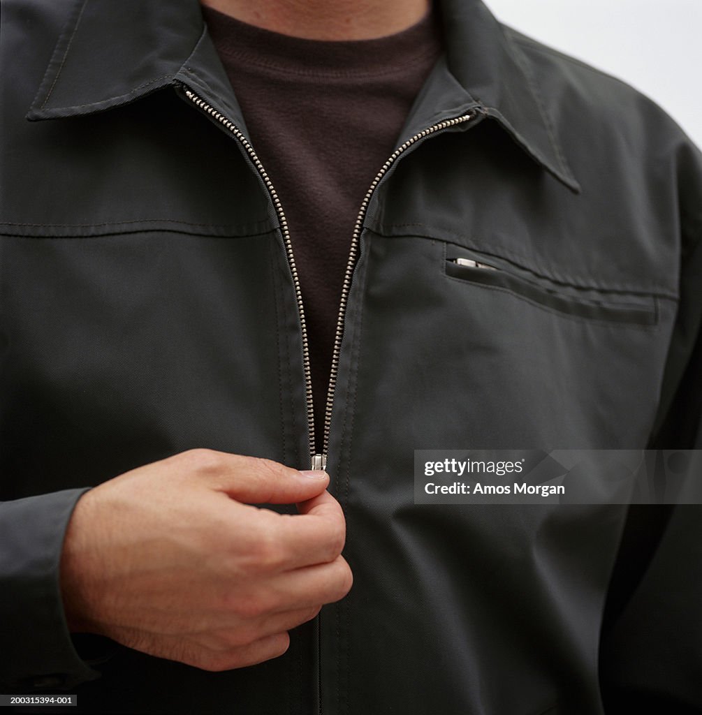 Man unzipping jacket, posing in studio, mid section, close-up