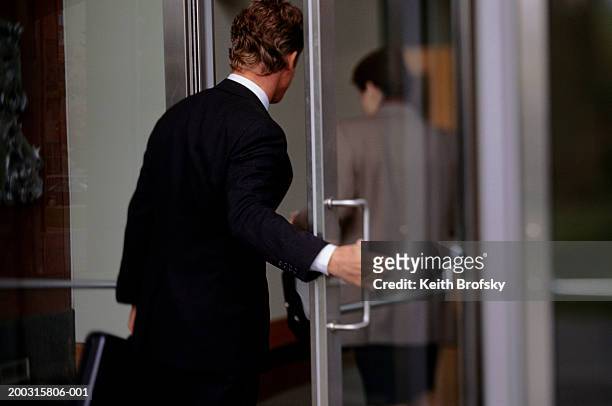 business people entering office through glass doors, (rear view) - entering stock pictures, royalty-free photos & images