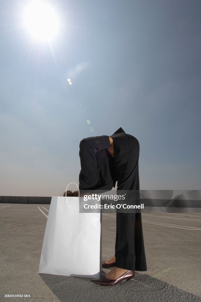 Woman in suit bending waist, head in shopping bag, side view