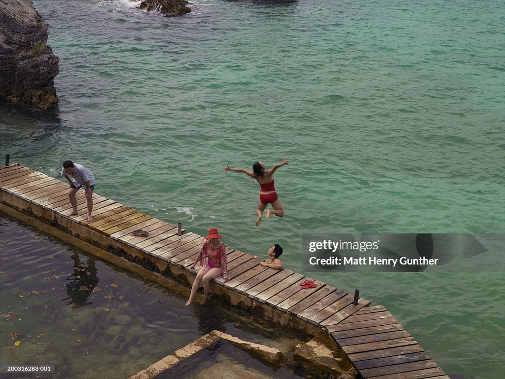Two couples relaxing on dock, woman jumping into water, elevated view