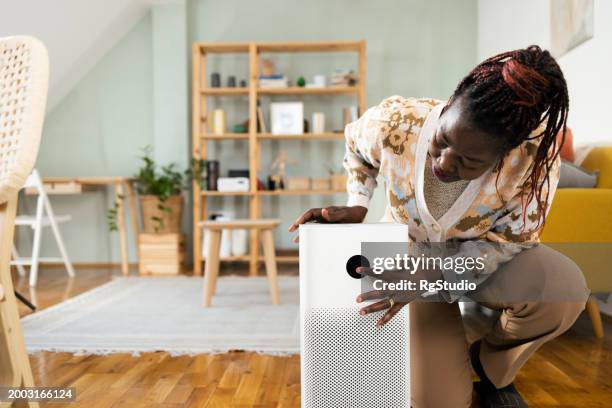 afroamerikanerin schaltet intelligenten luftreiniger ein - luftfilter stock-fotos und bilder