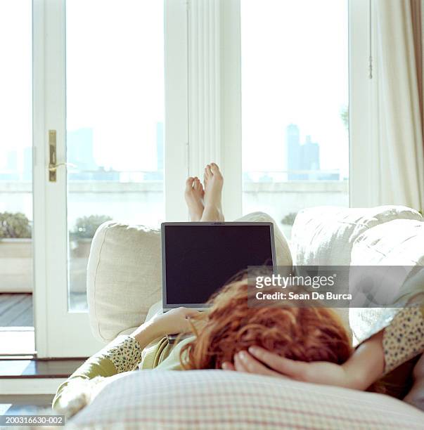 woman lying on sofa, using laptop, rear view - lying on back ストックフォ��トと画像