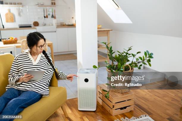 young asian woman turning on air humidifier using a digital tablet as a remote control - air purifier stock pictures, royalty-free photos & images